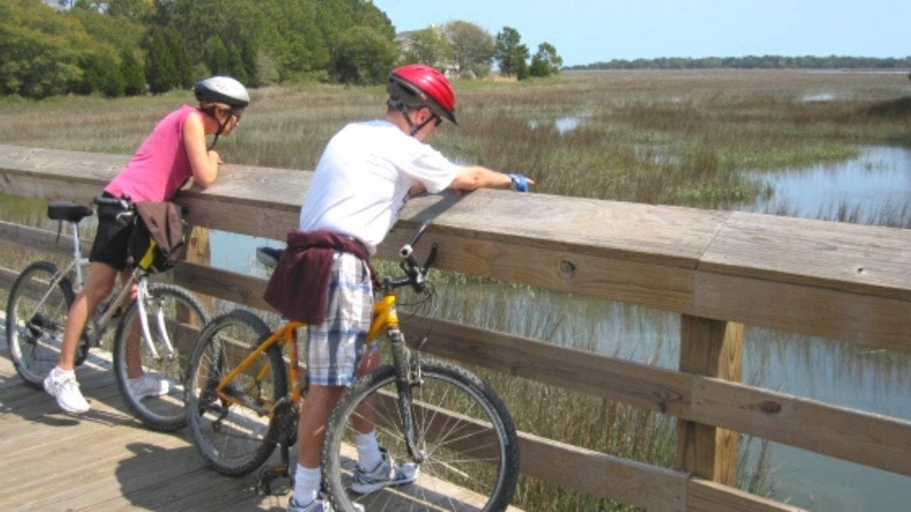 Man and woman riding bikes on bridge over marsh
